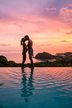 a young couple of men and women at a swimming pool during a vacation on a tropical island. man and woman in infinity pool during sunset. luxury vacation in Thailand pool of a luxury pool villa