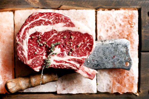 Bone In Rib Eye row Steak on pieces of salt on a wooden board. Stock image. Kitchen knife axe