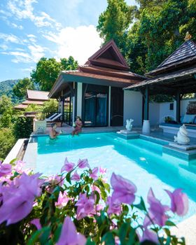 a young couple of men and women at a swimming pool during a vacation on a tropical island. man and woman in infinity pool during sunset. luxury vacation in Thailand pool of a luxury pool villa