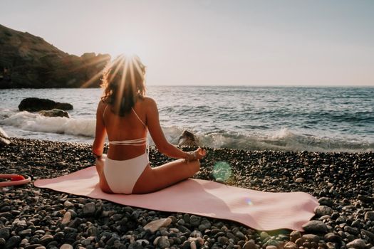 Young woman in swimsuit with long hair practicing stretching outdoors on yoga mat by the sea on a sunny day. Women's yoga fitness pilates routine. Healthy lifestyle, harmony and meditation concept.