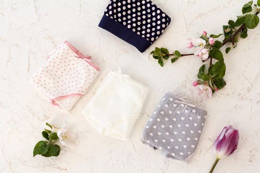 Folded cotton panties with a tulip and flowers of an apple tree on the white background. Woman underwear set. Top view.