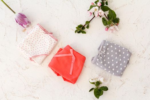 Folded cotton panties with a tulip bud and flowers of an apple tree on the white background. Woman underwear set. Top view.