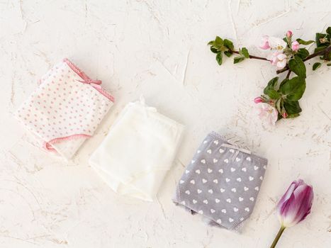 Folded cotton panties of different color with a tulip and flowers of an apple tree on the white background. Woman underwear set. Top view.