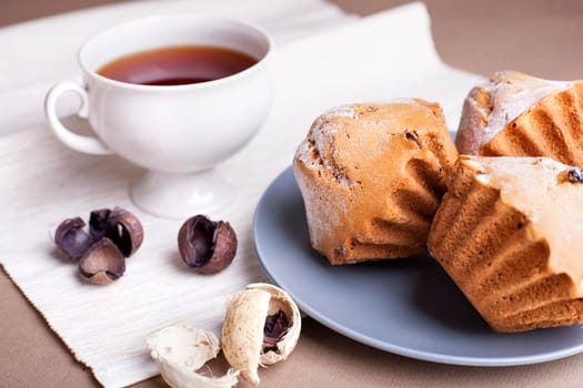 Muffin cakes and cup of tee on a grey plate. Beige - coffee background.