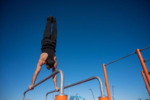 Shirtless man doing handstand on parallel bars at sports ground