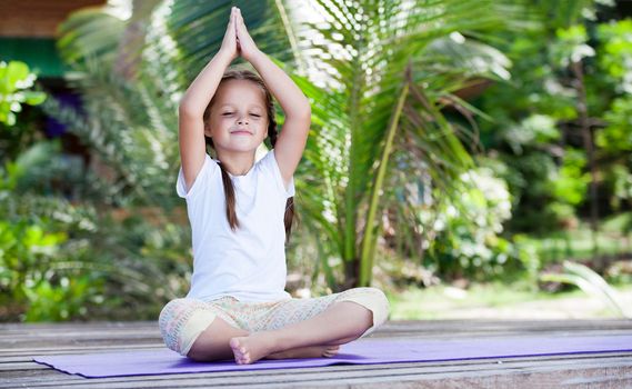 Child doing exercise on platform outdoors. Healthy ocean lifestyle. Yoga girl