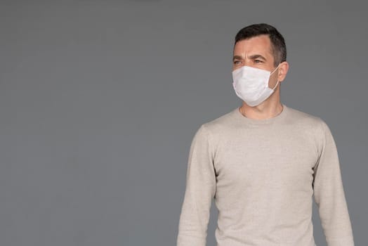 Young man wearing surgical white face mask and black gloves isolated on grey background with copy space