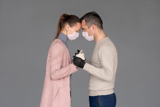 happy couple in love in repsiratory masks and gloves hugging each other isolated on grey background with copy space. Man and woman hold hands during the epidemic