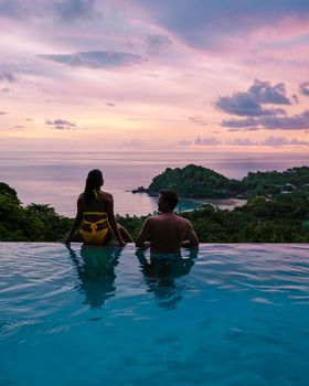 a young couple of men and women at a swimming pool during a vacation on a tropical island. man and woman in infinity pool during sunset. luxury vacation in Thailand pool of a luxury pool villa