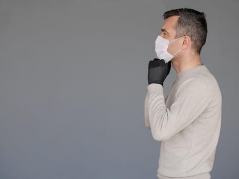 Young man wearing surgical white face mask and black gloves isolated on grey background with copy space