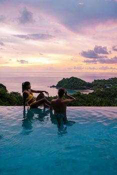 a young couple of men and women at a swimming pool during a vacation on a tropical island. man and woman in infinity pool during sunset. luxury vacation in Thailand pool of a luxury pool villa