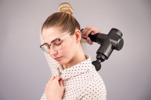 Caucasian business lady makes herself a back massage with a massager gun on a white background