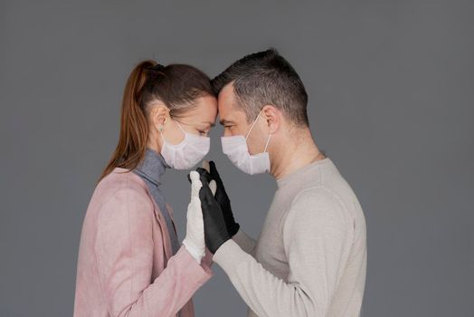 happy couple in love in repsiratory masks and gloves hugging each other isolated on grey background with copy space. Man and woman hold hands during the epidemic