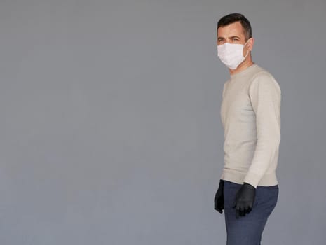 Young man wearing surgical white face mask and black gloves isolated on grey background with copy space