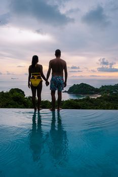 a young couple of men and women at a swimming pool during a vacation on a tropical island. man and woman in infinity pool during sunset. luxury vacation in Thailand pool of a luxury pool villa