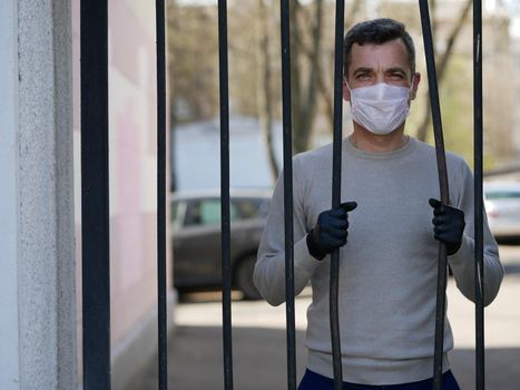 A man in white protective face mask near metal fence. Quarantine. Coronavirus concept. A man wearing protective mask. Pandemic covid