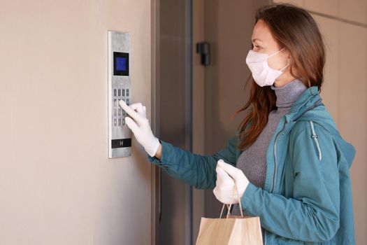 Woman wearing a mask for prevent virus with shopping bags dials the door code Portrait of beautiful happy woman near the door holding shopping bags