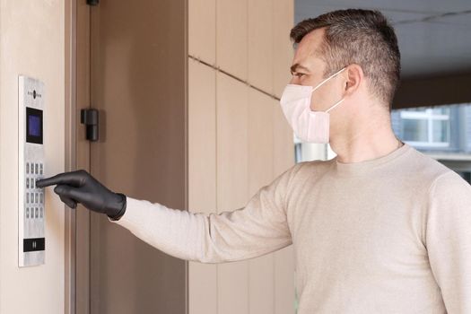 Man in face mask and gloves dials the code on the intercom and going in porch of his apartment. Pandemic covid-19 coronavirus concept