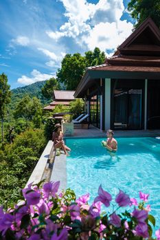 a young couple of men and women at a swimming pool during a vacation on a tropical island. man and woman in infinity pool during sunset. luxury vacation in Thailand pool of a luxury pool villa