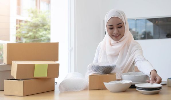 Muslim Business owner woman working online shopping prepare product packaging process at the office, young entrepreneur concept..