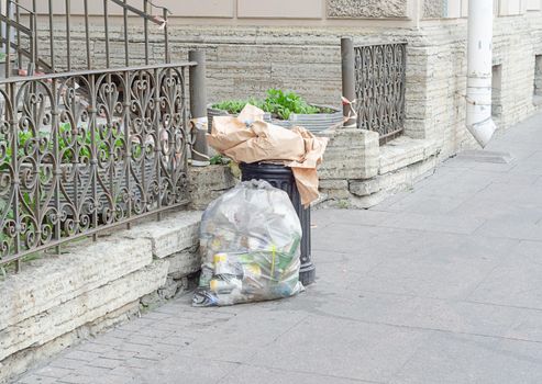 overflowing garbage litter bin and full plastic package with garbage in the street