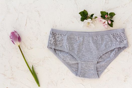 Gray cotton panties with a tulip and flowers of an apple tree on the white structured background. Woman underwear set. Top view.