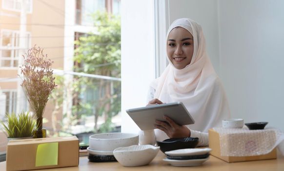 Entrepreneur Start-Up, Portrait of smiling female Muslim seller wearing hijab and hold the laptop. Concepts of E-commerce online shopping, Small delivery business from home.