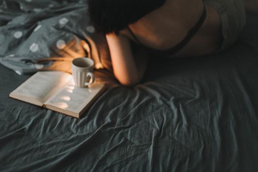 Young sexy woman portrait in bed with a book and coffee cup in the morning