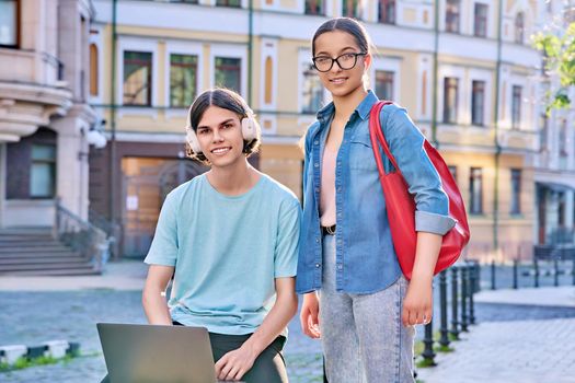 Teenage male and female using laptop for study, leisure, outdoor on city street. Guy and girl teenagers looking together at aptop screen. Lifestyle, technology, youth, education, city life concept