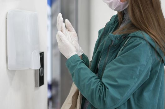 Washing hands in gloves using automatic sanitizer dispenser. Automatic sanitizer dispenser at supermarket. Coronavirus prevention. Coronavirus. Disinfectant in a shopping mall during the coronavirus epidemic.