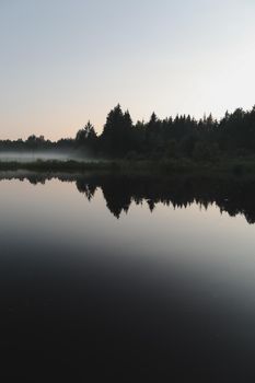 summer evening twilight view on picturesque plain lake surface with reflections of sky and trees.
