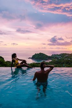 a young couple of men and women at a swimming pool during a vacation on a tropical island. man and woman in infinity pool during sunset. luxury vacation in Thailand pool of a luxury pool villa