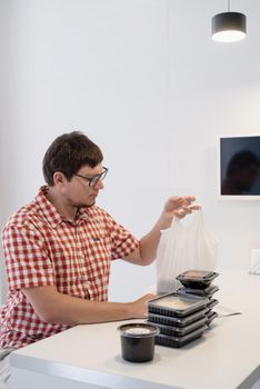 Delivery food, products to home. Shopping and healthy food concept. Young man in red plaid shirt Young man sorting food delivery boxes at the modern kitchen at the modern kitchen