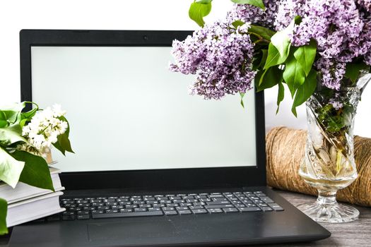 Lilac flower bouquet in glass vase with open laptop white screen and books, rope, copy space for text, springtime, blossom