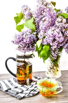 fresh herbal tea cup, teapot and blossom Violet lilac flowers bouquet in glass vase, Kitchen interior decorations. Mother's day congratulation,