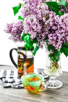 fresh herbal tea cup, teapot and blossom Violet lilac flowers bouquet in glass vase, Kitchen interior decorations. Mother's day congratulation,