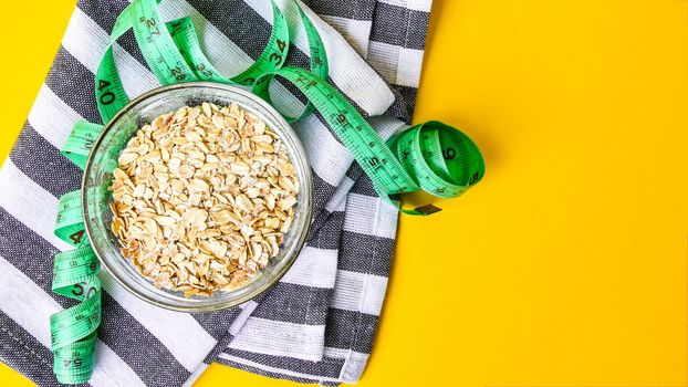 Oatmeal in a bowl and green centimeter tape on bright yellow background with kitchen towel, copy space, quick healthy breakfast
