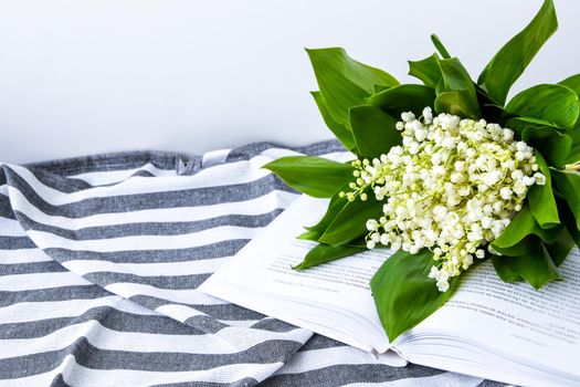 Bouquet of a white lilies of the valley on the open book on the towel in strip, soft focus. Spring flowers education, and reading, stay home