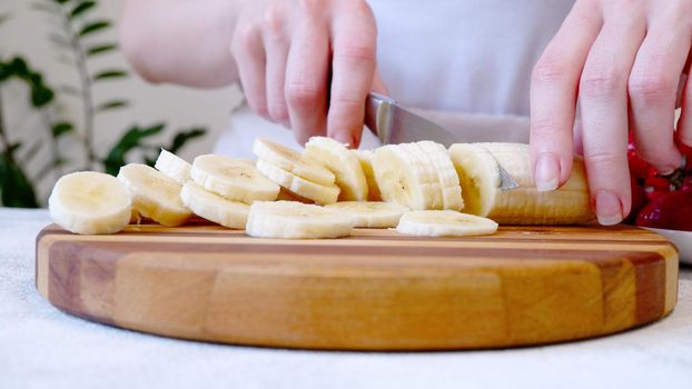 Woman cutting banana on wooden board and preparing smoothie or milkshake.