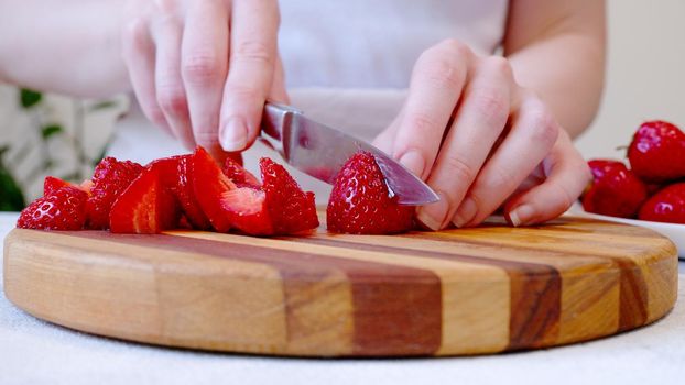 Woman cutting strawberrys on wooden board and preparing smoothie or milkshake.
