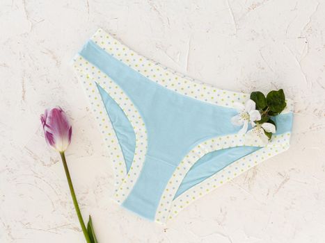 Blue cotton panties with a tulip and flowers of an apple tree on the white structured background. Woman underwear set. Top view.
