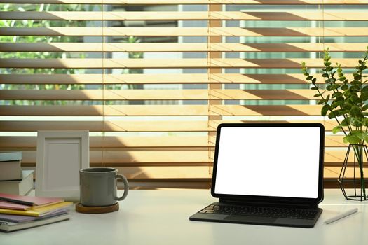 Digital tablet with wireless keyboard, coffee cup, books and picture frame on white table.