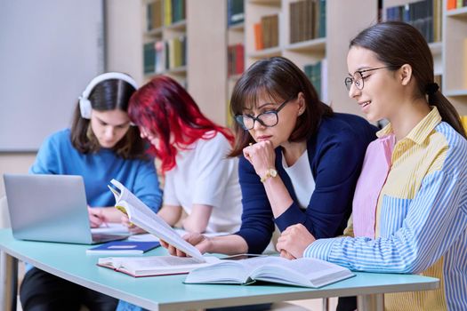 Group of teenage students study in school library classroom. Teen girl and female teacher mentor helping in their studies. High school, learning, education, knowledge, adolescence