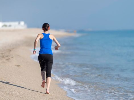 young woman runs on a seashore sandy beach in the morning