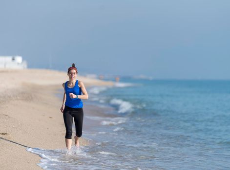 young woman runs on a seashore sandy beach in the morning