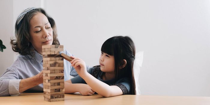 Little girl with her grandma playing jenga game at home.