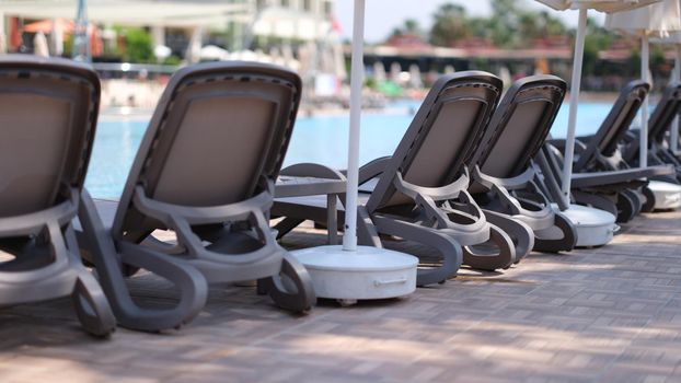 Many empty sun loungers and parasols standing near swimming pool. Vacation at resort concept