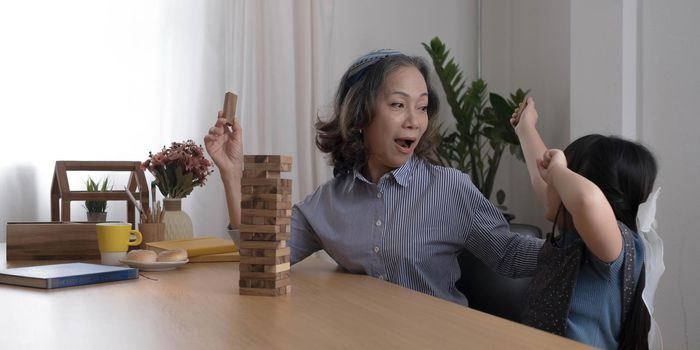 Happy moments of Asian grandmother with her granddaughter playing jenga constructor. Leisure activities for children at home..