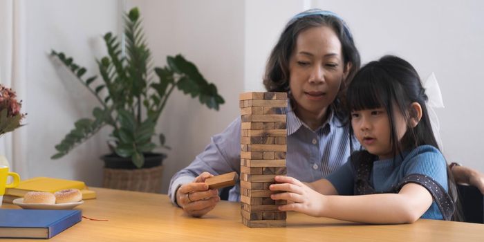 Happy moments of Asian grandmother with her granddaughter playing jenga constructor. Leisure activities for children at home..