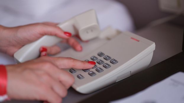 Female hands with red manicure dialing phone number closeup. Hotel service concept
